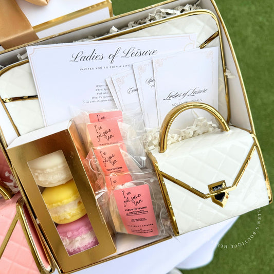 Gift set with a white handbag shaped mug set and saucer, macaron candles, and organza gloves and daily ritual cards. wrapped in white and gold gift box.