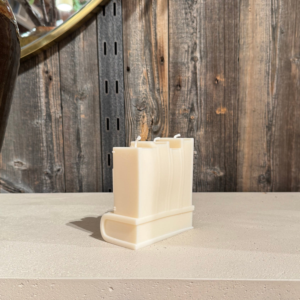 A cream-colored book shaped candle, displayed on a light stone countertop against a rustic wood-paneled wall.