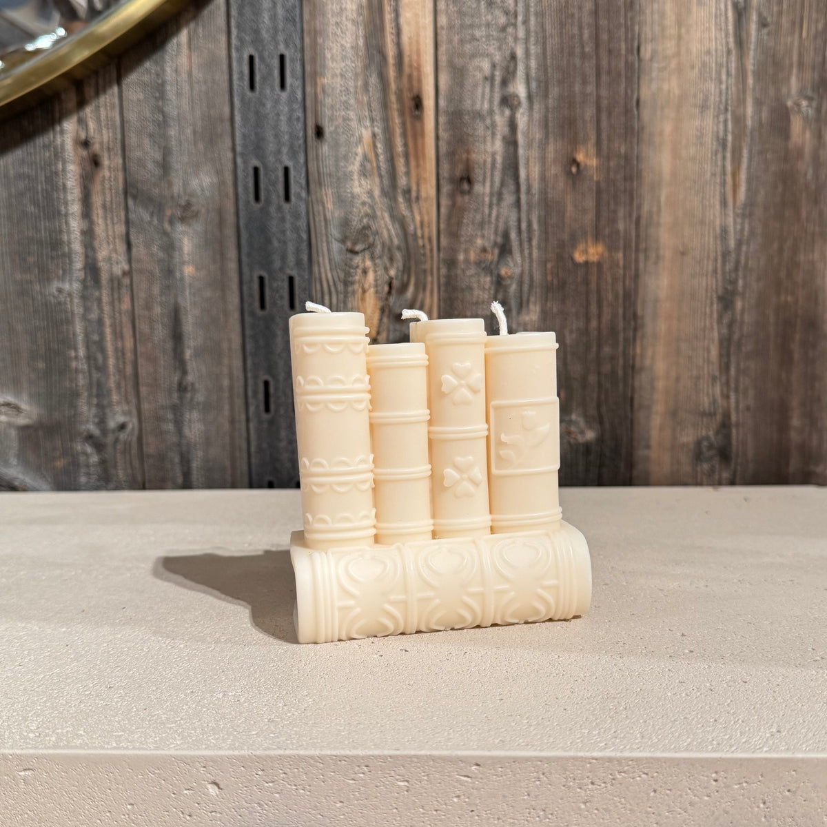five cream-colored book shaped candles shaped like vintage books, arranged on a light stone surface against a rustic dark wood plank wall.